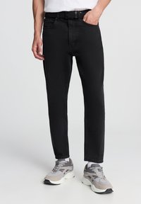 Jeans in denim nero con una vestibilità dritta, design a cinque tasche e una cintura, abbinati a scarpe da ginnastica grigie e bianche.