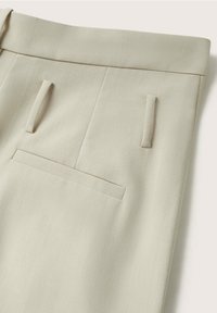 Pantalon beige clair sur mesure montrant la ceinture, les passants de ceinture et deux poches sur une surface plane.