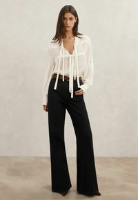 Valge triibuline pluus lipsu detailiga ja pika varrukaga, kombineeritud kõrge vöökohaga mustade laia säärtega pükstega ning pruuni vööga. Siledad tekstuurid.