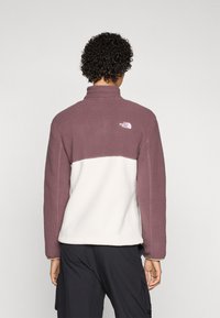 Fleece pullover met een hoge kraag, voorzien van een bordeauxrode en witte kleurblokontwerp. Zachte textuur en het North Face-logo op de achterkant.