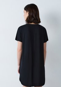 Vestito nero a maniche corte con scollatura arrotondata, vestibilità rilassata e spacchi laterali per facilitare i movimenti. Tessuto dalla trama liscia.