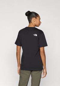 Μαύρο βαμβακερό t-shirt με κοντά μανίκια, με λευκό λογότυπο στο πάνω μέρος της πλάτης. Η εφαρμογή είναι άνετη, με στρογγυλή λαιμόκοψη.