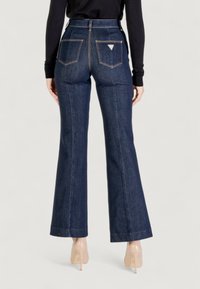 Jeans a zampa d'elefante in denim blu scuro con vita alta, cuciture visibili, due tasche posteriori e un piccolo dettaglio con logo sopra la tasca destra.