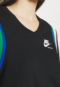 Detailní záběr na osobu v černém sportovním tričku Nike s rukávy pruhovanými zelenou, modrou a růžovou barvou a výstřihem do V.