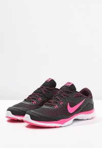 Scarpe da ginnastica nere e rosa con una tomaia in mesh testurizzato, lacci rosa e una suola bianca. Presenta un prominente logo Nike rosa sul lato.