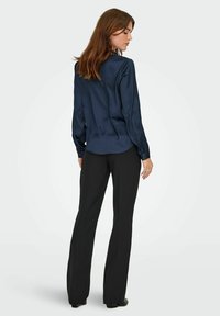 Navy satin shirt met lange mouwen en knoopmanchetten, gecombineerd met zwarte op maat gemaakte broeken. Gladde textuur, klassieke kraag en subtiele glans.