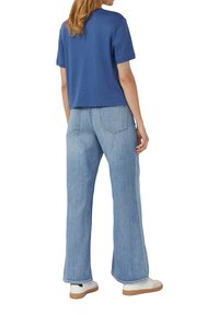 T-shirt bleu à manches courtes associé à un jean large bleu clair, offrant une coupe décontractée, et des baskets blanches avec des semelles beiges.