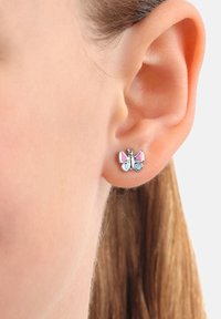 Silverfärgad fjärilssmycke med rosa och blå emalj som bärs på någons örsnibb mot en enfärgad bakgrund.