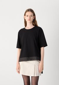 Black short-sleeve t-shirt with a loose fit, featuring a satin-like lower panel and round neckline, paired with a light-colored skirt.