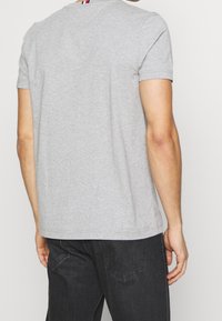 Camiseta de algodón gris con mangas cortas y escote redondo. Presenta una franja multicolor en la parte posterior del cuello. Corte simple y clásico.