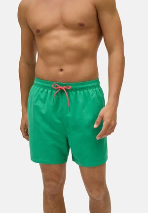 Bañadores verdes con cinturilla elástica y cordón rosa. Tejido suave, longitud por encima de la rodilla, sin patrones ni acentos adicionales.