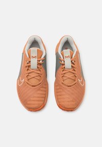 Para pomarańczowych siateczkowych butów sportowych z szarymi akcentami, białym wnętrzem, białym logo w kształcie łyżwy i sznurowadłami związanymi w kokardki, widziane z góry.