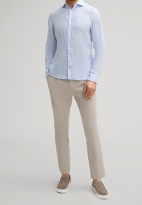 Chemise en lin bleu clair à manches longues, boutonnée à l'avant, associée à un pantalon en lin beige et des chaussures marron texturées à enfiler.