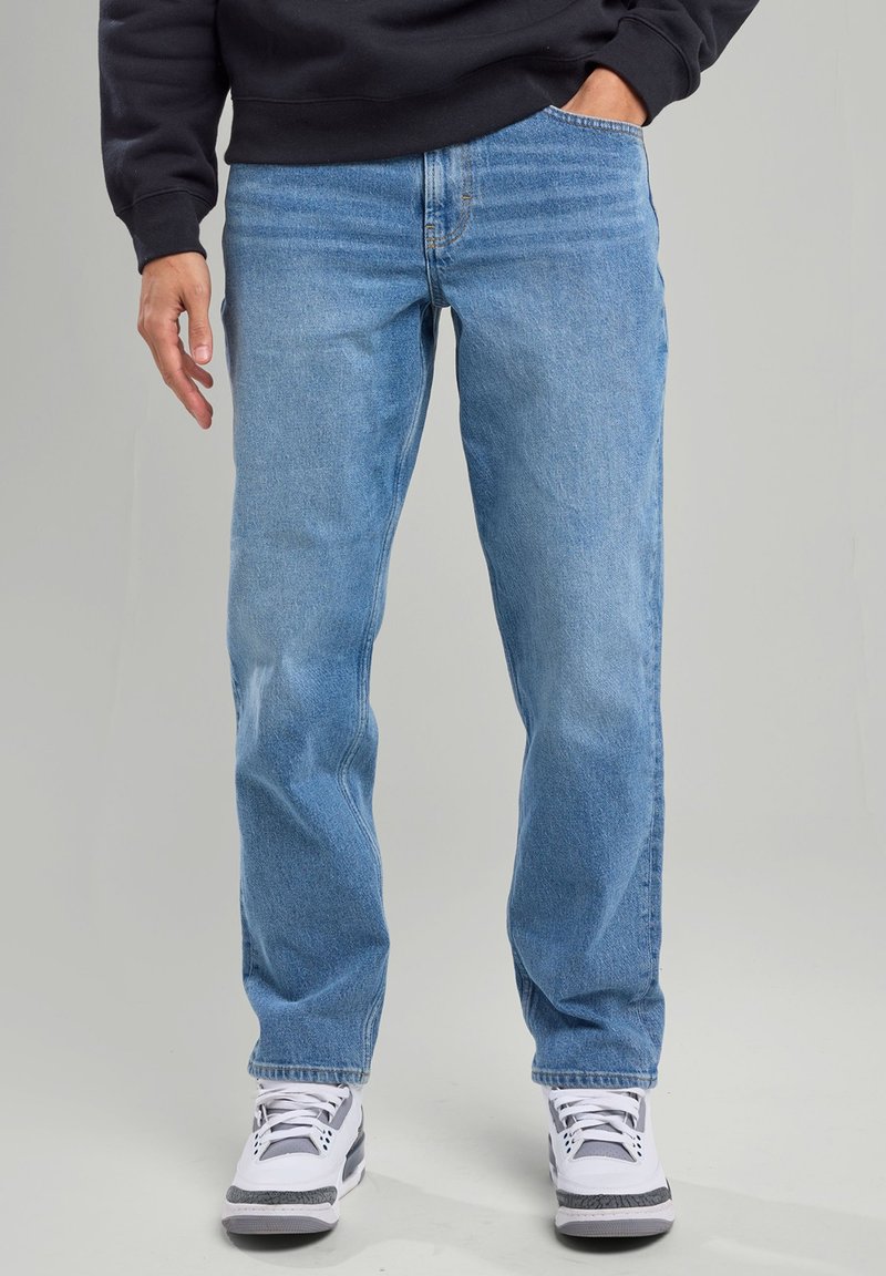 Light blue denim jeans with straight-leg fit, featuring subtle fading and five-pocket design, worn with white sneakers.