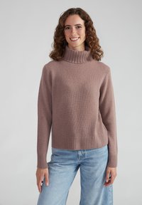 Hellblauer Turtleneck-Pullover aus weichem, strukturiertem Stoff in mauve. Rippbündchen und Saum mit lockerer Passform. Kombiniert mit hellblauen weit geschnittenen Jeans.