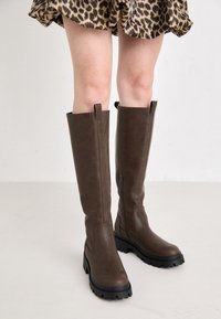 Bottes montantes marron en similicuir texturé, dotées d'une semelle en caoutchouc robuste et d'une fermeture éclair latérale pour un enfilage facile.