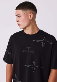 Zwarte T-shirt van katoen, versierd met zilveren geborduurde sterren en een logo in het midden. Korte mouwen met een relaxte pasvorm.
