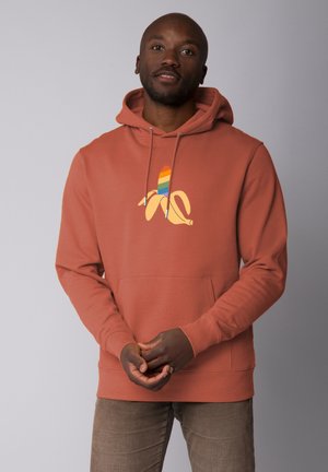 Rust-colored hoodie with a front pocket and drawstring hood, featuring a yellow banana graphic with rainbow stripes. Soft fabric texture.
