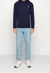 Námořnická mikina s přední kapsou a šňůrkou, spárovaná s světle modrými rovnými džíny a bílými teniskami s modrými akcenty.