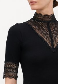 Czarny, prążkowany top z wysokim koronkowym kołnierzem i koronkowymi rękawami o krótkiej długości, zdobiony misternymi wzorami w detalach koronkowych.