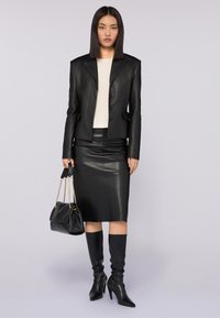 Chaqueta de cuero negra con un diseño estructurado, una falda de cuero negro ajustada, botas de tacón negras hasta la rodilla y un bolso negro con acentos dorados.