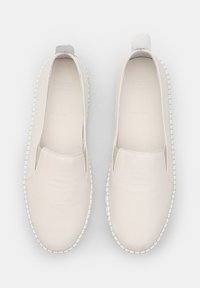 Fehér bőr slip-on cipők lekerekített formával, texturált kiemeléssel a sarkon és varrott talppal, amely kontrasztos széllel rendelkezik.