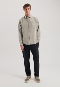 Cămășă călcată de culoare gri deschis, cu un singur buzunar pe piept, asortată cu pantaloni negri și adidași bej. Material neted, croială ajustată.