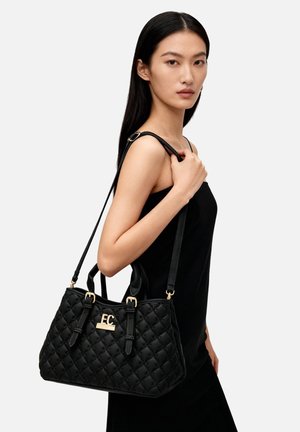 Borsa nera trapuntata con ferrature e logo dorate, dotata di doppi manici e tracolla removibile. Texture liscia e forma strutturata.