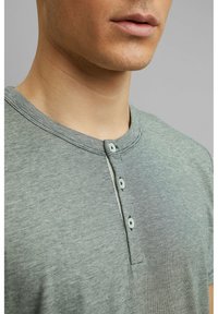 Grijze, gestreepte korte mouwen henley shirt met een ronde hals en een drie knopen sluiting. Zachte stof met subtiele textuur en contrasterende stiksels.