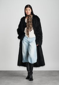 Fekete műszőrme kabát, mintás sál, fekete felső és világoskék, bővölgyű farmernadrág. Fekete térdig érő csizmák. Puha textúra és merész dizájnelemek.