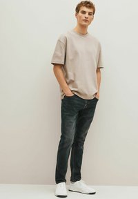 Beige T-shirt med korte ærmer, mørke jeans og hvide sneakers. T-shirten har en rund halsudskæring og en afslappet pasform; jeansene har en klassisk pasform og minimal slid.