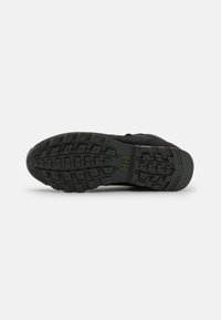 Suela de zapato deportivo negro con goma texturizada para agarre, que presenta un patrón de banda de rodadura y una ligera curvatura para brindar soporte.