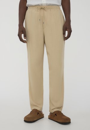 Pantaloni beige leggeri con cintura elastica e cordino. Design a gamba dritta con tasche laterali. Scarpe slip-on in suede marrone.