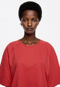 Camiseta de algodón roja con un corte relajado y mangas raglán. Textura suave y escote redondo, diseñada para un uso casual.