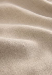 Tessuto di lino beige con superficie morbida e strutturata, che mostra onde dolci e sottili fibre naturali per una qualità leggera e traspirante.