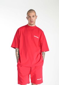 Conjunto de camiseta roja de gran tamaño y pantalones cortos, hecho de tela suave. Presenta un cuello redondo y el logo blanco "MULTIPLY" en el pecho.