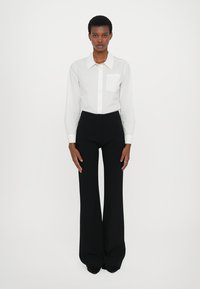 Witte langsliggende knopsluiting shirt met een borstzak, gecombineerd met hoge zwarte flared broek. Glad materiaal, op maat gemaakte pasvorm.
