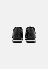 Musta lenkkitossut, joissa on tekstuuri krokotiilikuosi, mokkanahkaosiot ja valkoinen ulkopohja, joka on matala.