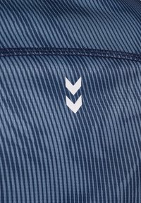 Närbild av blårandigt tyg med mörkblå söm och två vita nedåtriktade sicksackpilar i mitten.