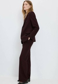 Vinrød jakkesæt med en tætsiddende blazer og bukser med vide ben, lavet af et tekstureret stof, med to knapper og diskrete skrædderdetaljer.