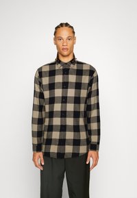 Camisa de manga larga abotonada en un patrón a cuadros en negro y beige, hecha de una tela suave, con un collar puntiagudo y botones negros.