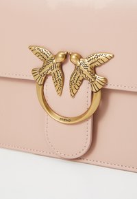 Roze leren handtas met een gouden ring als sluiting, versierd met twee gestileerde vogels. Gladde textuur met gestikte details.