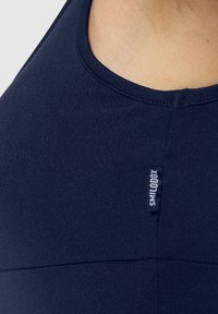 Sujetador deportivo en color navy con un tejido suave y elástico, un escote redondeado y una pequeña etiqueta de marca en la costura lateral.