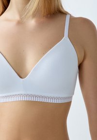 Bra triangolare bianco realizzato in tessuto morbido, con un delicato bordo in pizzo lungo la fascia inferiore, dotato di spalline sottili e regolabili.