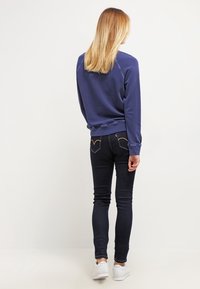 Marineblauwe sweatshirt met geribbelde mouwen, gecombineerd met slim-fit zwarte jeans met een achterzakontwerp en witte sneakers.