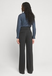 Camicia blu navy con bottoni e maniche lunghe, abbinata a pantaloni neri a gamba larga a vita alta con tasche posteriori.