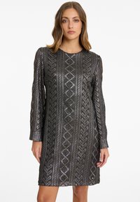Schimmerndes schwarzes Kleid mit langen Ärmeln, aus strukturiertem Stoff mit komplizierten geometrischen Mustern und gerader Silhouette.