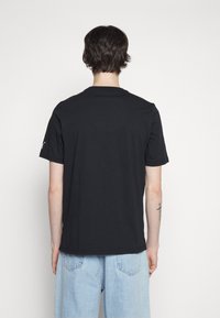 Svart bomullströja med klassisk rund hals och korta ärmar, med en liten logotyp på vänster axel.