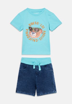 Lyseblå t-skjorte for småbarn med bjørn som har på solbriller og teksten "Guess Los Angeles California", kombinert med mørkeblå shorts med snøring.
