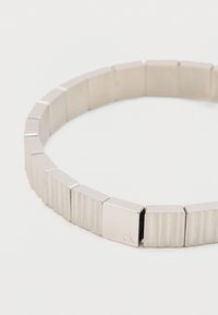 Brăţară argintie compusă din verigi plate, rectangulare, cu suprafeţe alternante netede şi texturate, având o mică gravură „ck” pe una dintre verigi.